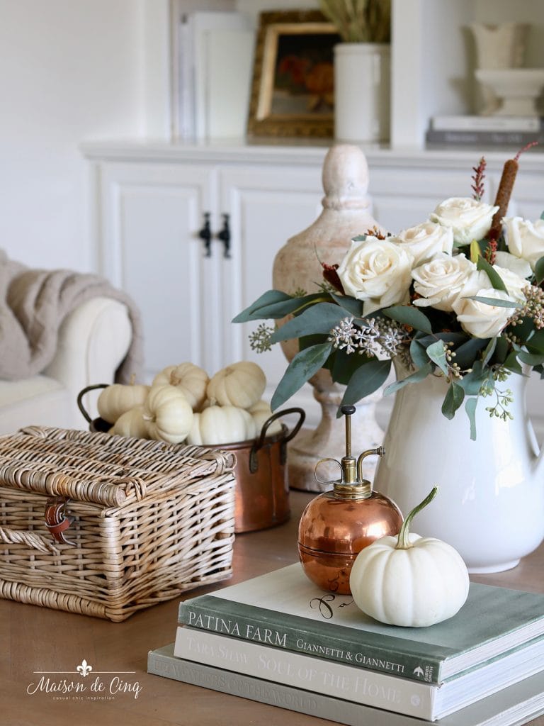 Elegant coffee table vignette with flower pitcher, stacked books, mini white pumpkins